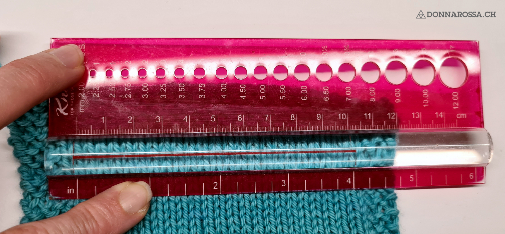 knitted swatch in turquoise is measured with a pink ruler